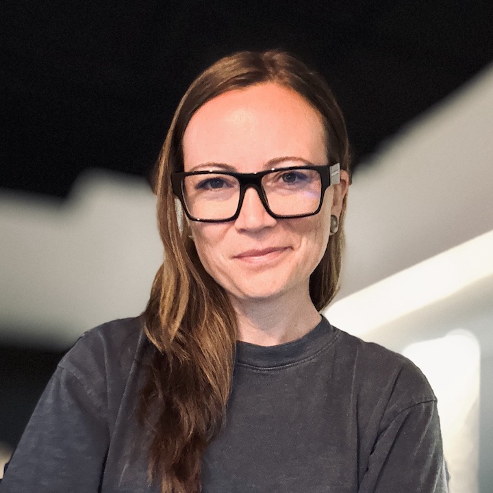 Lindsay X Moore, wearing black-framed glasses and a charcoal shirt.